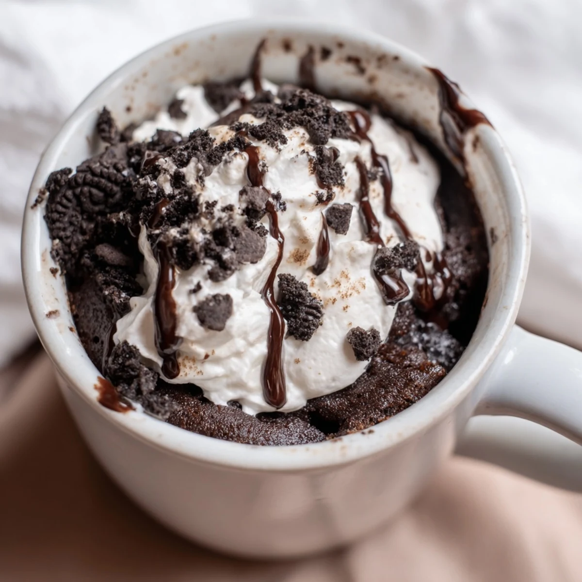 Close-up shot shows a freshly made Oreo Mug Cake, warm and ready to eat with a creamy topping.