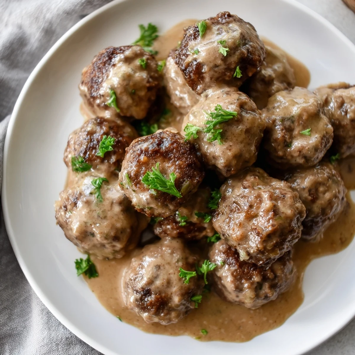 A close-up of tender Swedish Meatballs, showcasing their rich color and nestled in luscious, thick sauce.