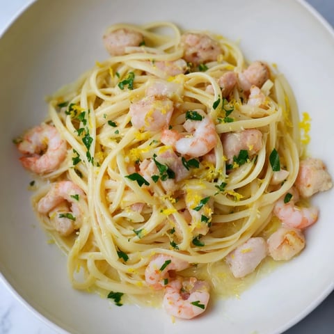 A close-up of Lemon Garlic Shrimp & Chicken Pasta twirled on a fork, showcasing tender shrimp and chicken in a glossy lemon-butter sauce with fresh parsley garnish.