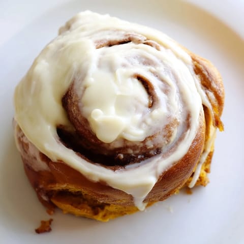 Golden-brown pumpkin cinnamon rolls swirled with cinnamon sugar and creamy frosting, ready to serve for breakfast.  