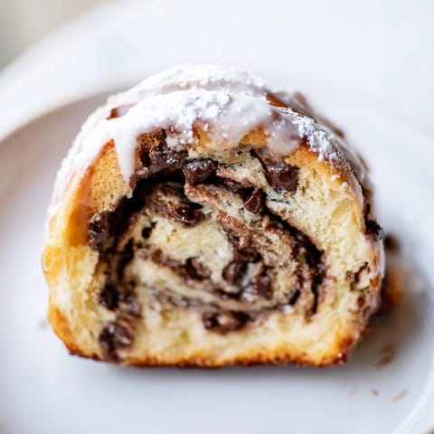 A close-up view of a glazed Nutella Chocolate Chip Roll showing the gooey, rich hazelnut spread and chocolate filling inside.