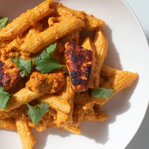 A vibrant plate of chicken tikka pasta garnished with fresh cilantro, served alongside garlic naan for dipping.