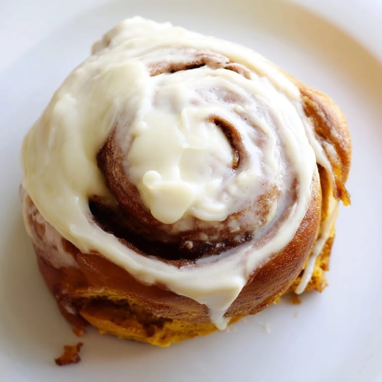 Golden-brown pumpkin cinnamon rolls swirled with cinnamon sugar and creamy frosting, ready to serve for breakfast.  